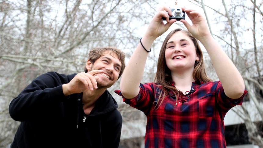 Talua Tawhai holds a camera above her head while Greg Lewis points from the side