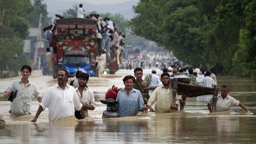 Residents carry their belongings through a flooded road in Risalpur, located in Nowshera district