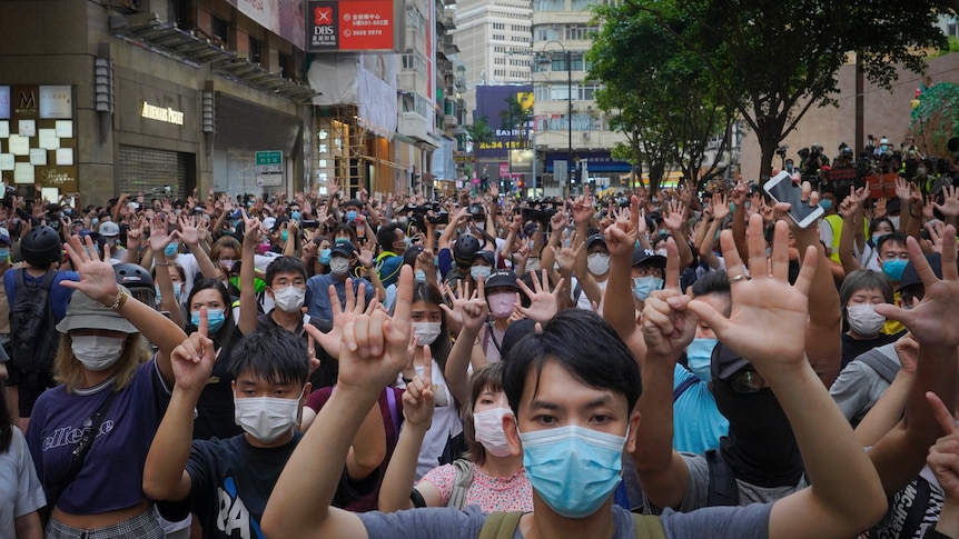 Hundreds of people stand in a Hong Kong street holding up their hands.