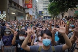 Hundreds of people stand in a Hong Kong street holding up their hands.
