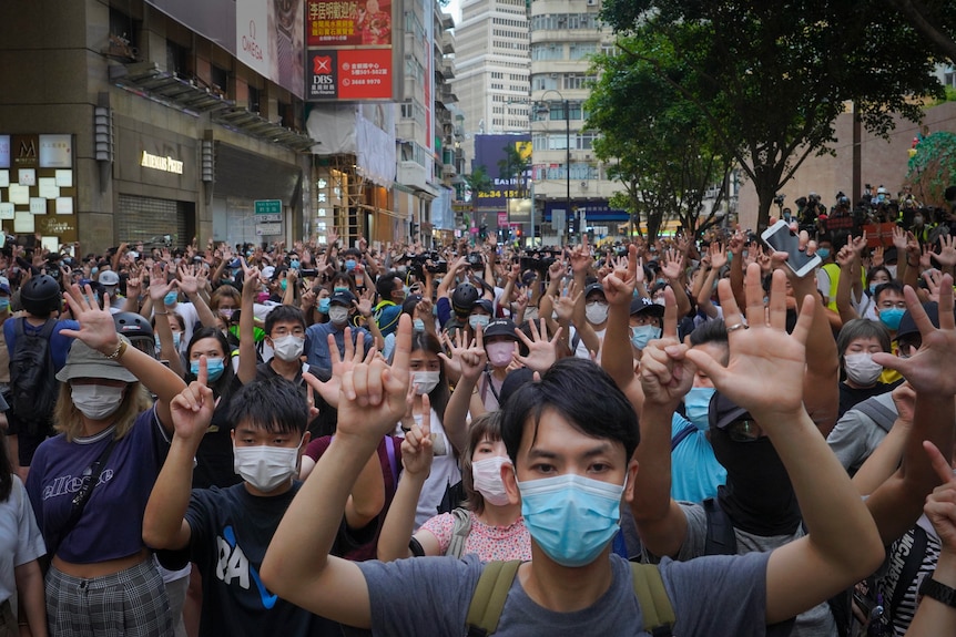 Setki ludzi stojących na ulicy w Hongkongu, podnoszące ręce.