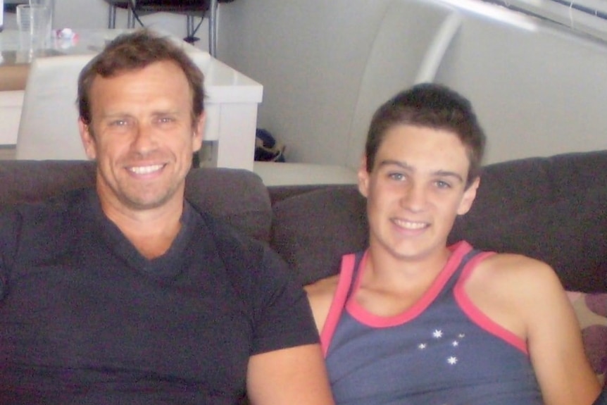 A man and younger looking teenager sitting together on a couch.
