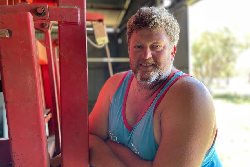 A man in a blue singlet leans against a red wool press.