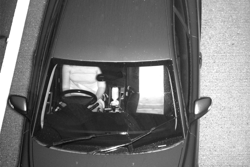 An aerial black and white photo of a person wearing their seatbelt incorrectly.