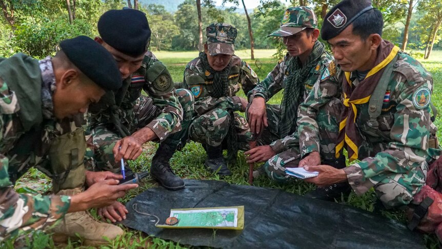 Thai men in paramilitary gear crouch on the ground inspecting a map