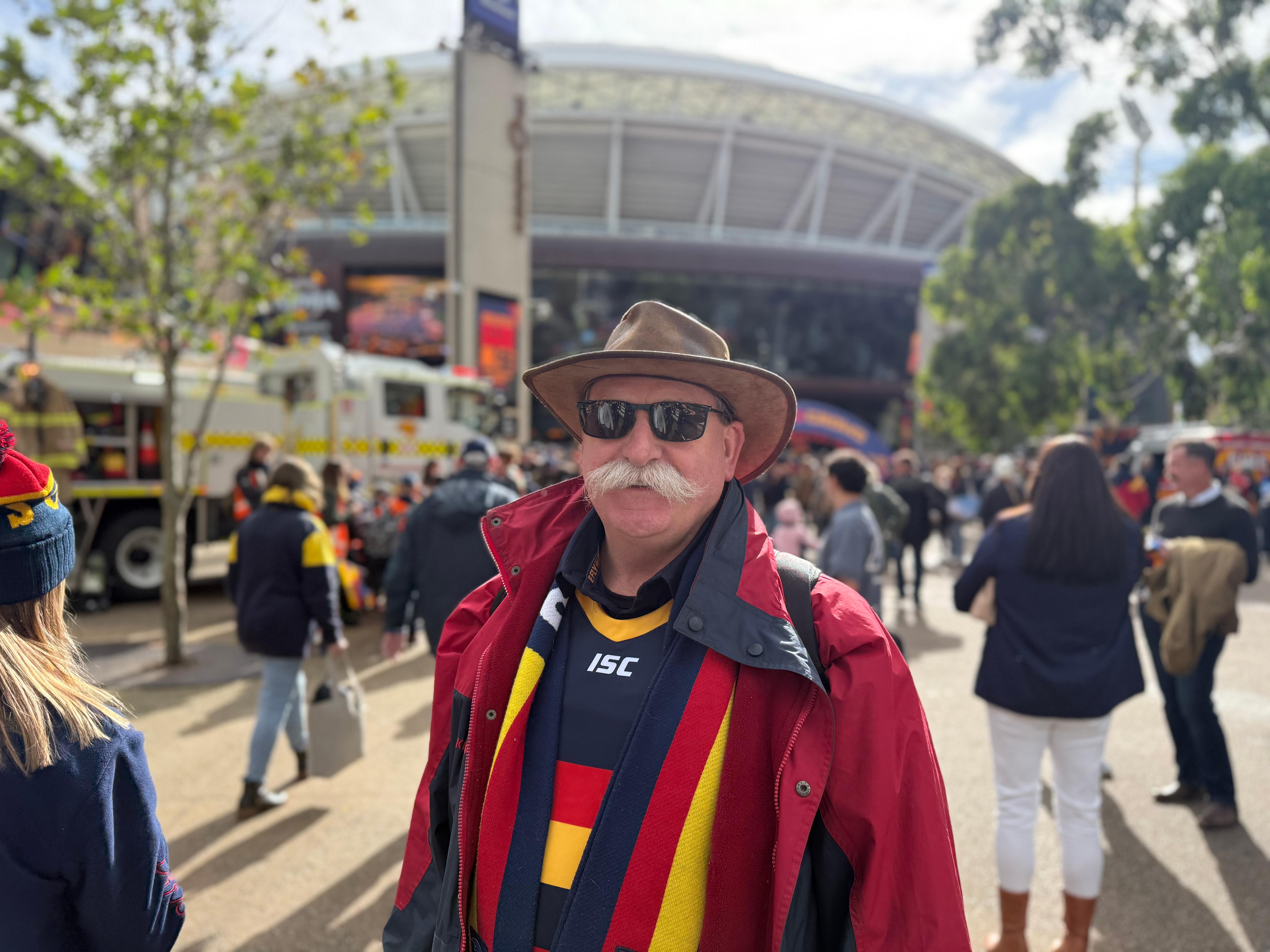 A man with a moustache wearing Crows gear in the forecourt of Adelaide Oval