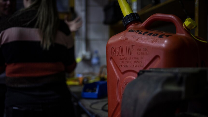 A close up of a jerry can and a woman in the background with her back to the camera.