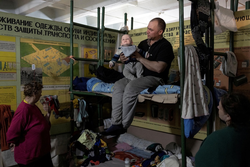 a man holds a baby on a makeshift bed inside a bunker