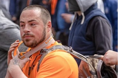 A man in an orange shirt at a protest.