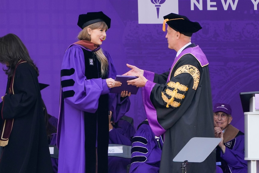 Woman in university gowns receives folder from man. 