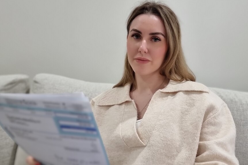 A woman sits on a sofa holding a bill.