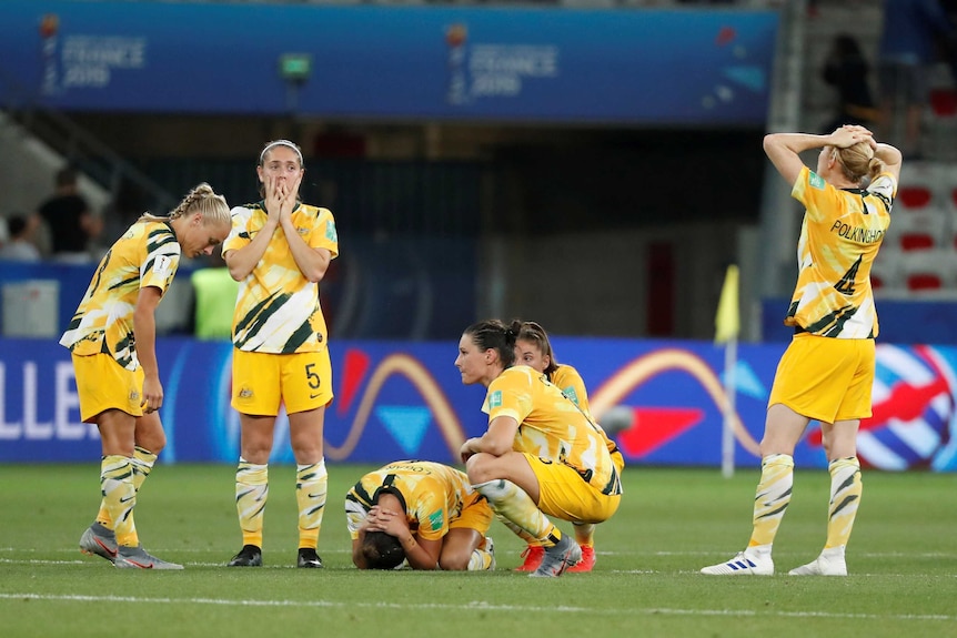 A group of women's international footballers kneel and crouch on the ground after a World Cup loss.