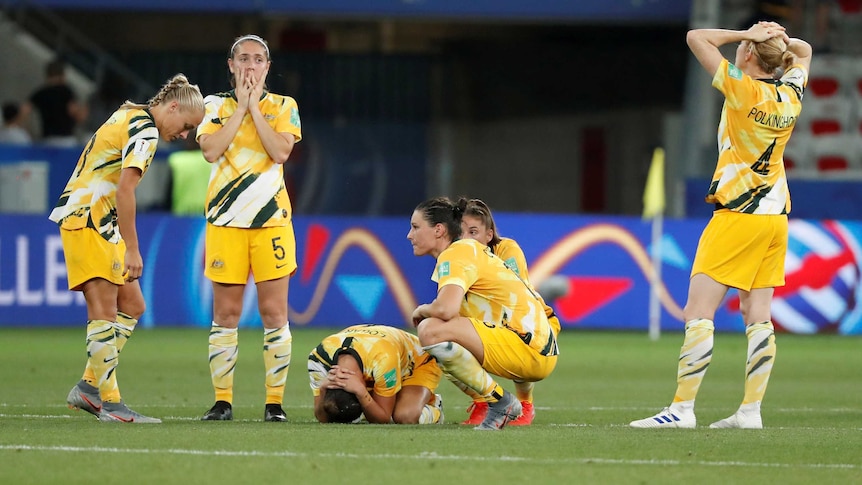 A group of women's international footballers kneel and crouch on the ground after a World Cup loss.