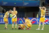 A group of women's international footballers kneel and crouch on the ground after a World Cup loss.