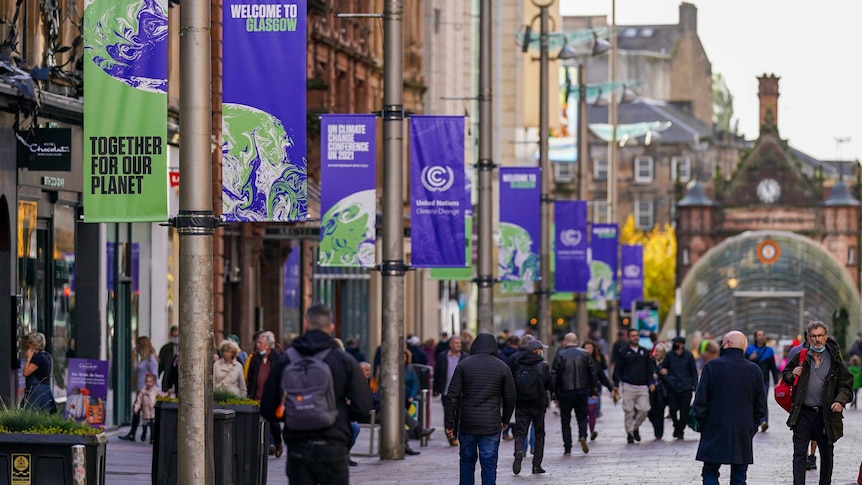 street scene, people walking, banners saying 'welcome to Glasgow' + 'together for our planet'