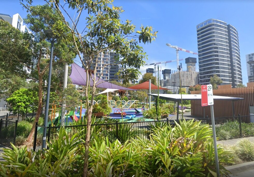 A screenshot from Google Street View shows a park in front of apartment buildings
