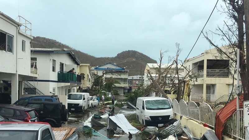 A street in St Martin with broken fences and collapsed trees.