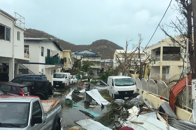A street in St Martin with broken fences and collapsed trees.