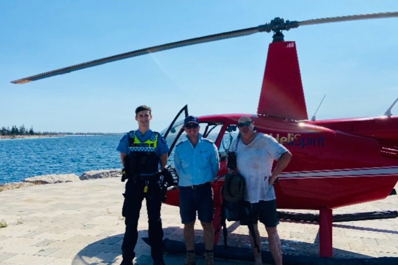 A police officer and a pilot stand beside a helicopter with a middle-aged man.