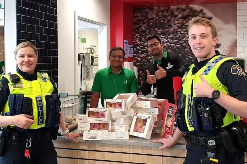 Two police officers give the thumbs up in front of boxes of donuts