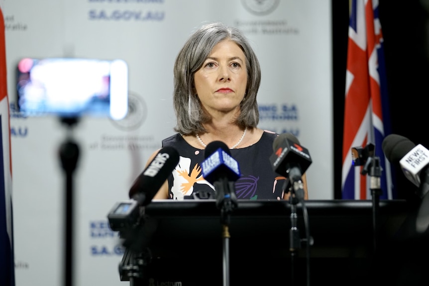 Nicola Spurrier stands in front of a lectern, facing the cameras and media equipment filming her in the foreground