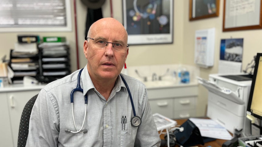 A doctor sitting at his desk with a stethoscope around his neck.