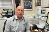 A doctor sitting at his desk with a stethoscope around his neck.