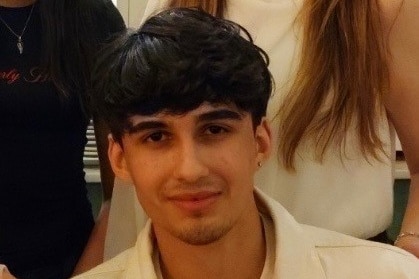 A teenager smiling while earing a white jacket.