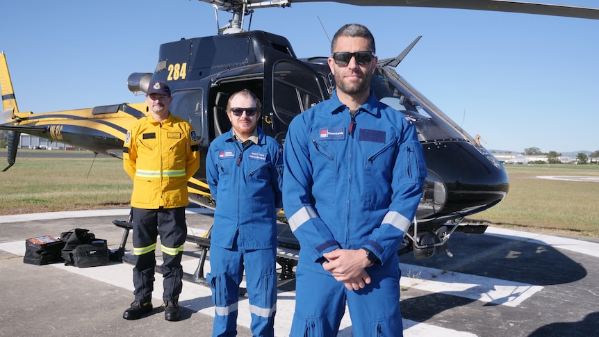 three men in protective uniform stand in front of helicopter