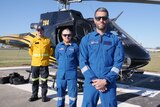 three men in protective uniform stand in front of helicopter