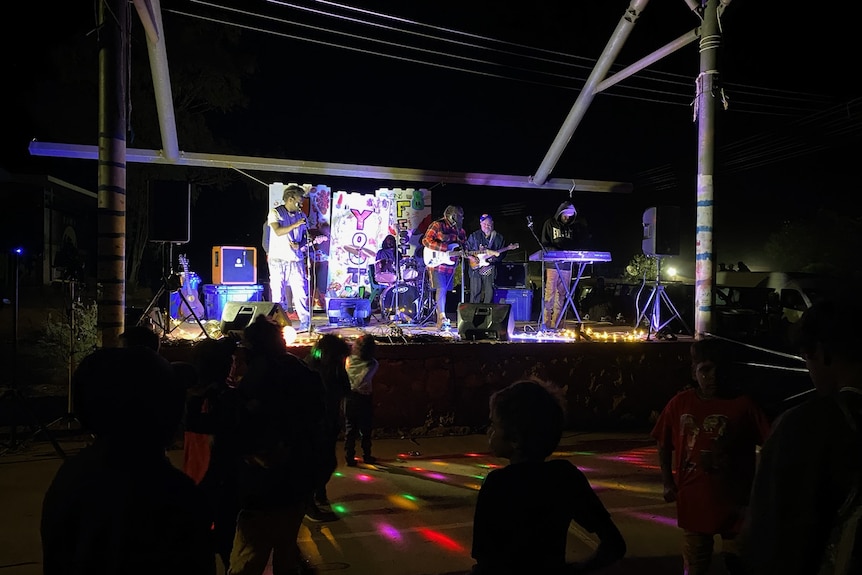 Kids stand in front of a stage as a band plays at night