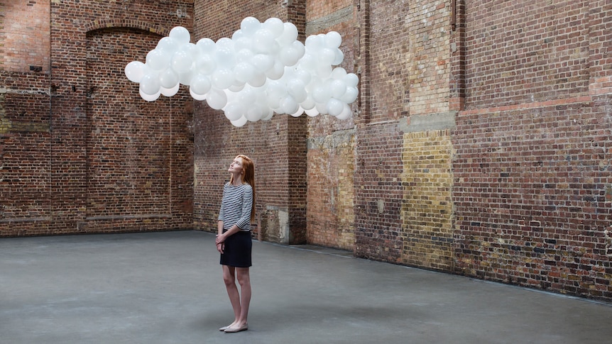 Woman in warehouse, cloud of balloons above head