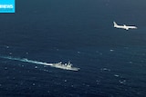 An aerial photo showing a Navy ship in the open ocean, with a military jet flying overhead.
