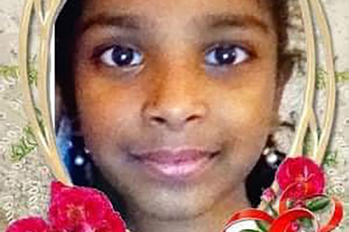 Une balle dans la tête d'une jeune fille souriante dans un cadre avec des fleurs rouges autour d'elle.