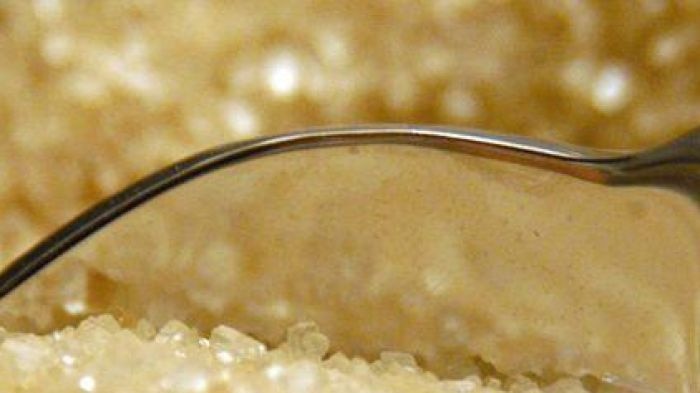 A spoon sits in a bowl of raw sugar