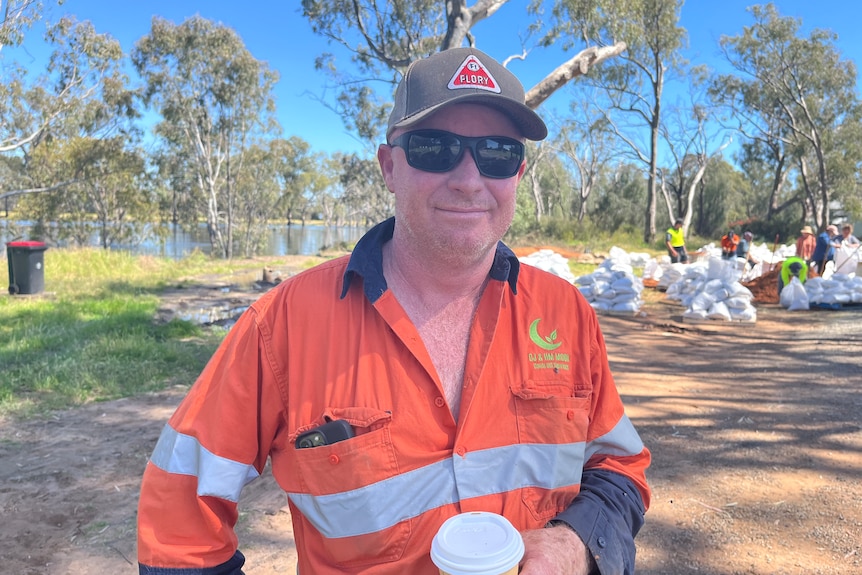 A man in organ hi-vis by the Murray River. In the background are stacks of sandbags.