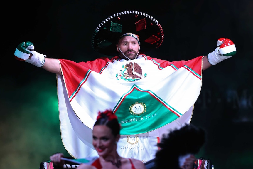 A boxer comes to the ring wearing a poncho and sombrero in Mexican colours.
