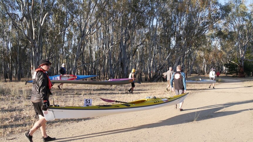 Men carry kayaks along a track for the start of the Massive Murray Paddle
