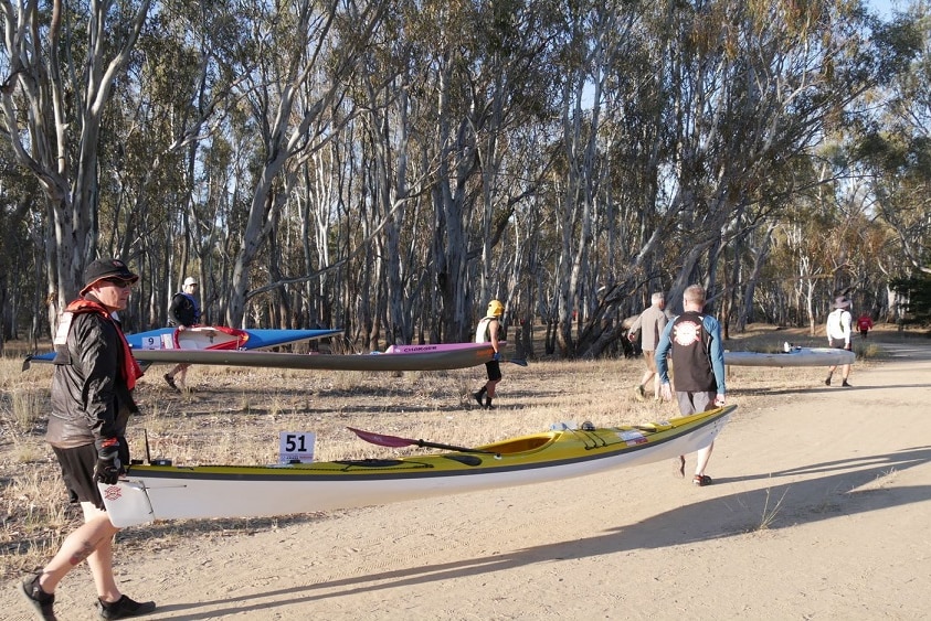 Men carry kayaks along a track for the start of the Massive Murray Paddle