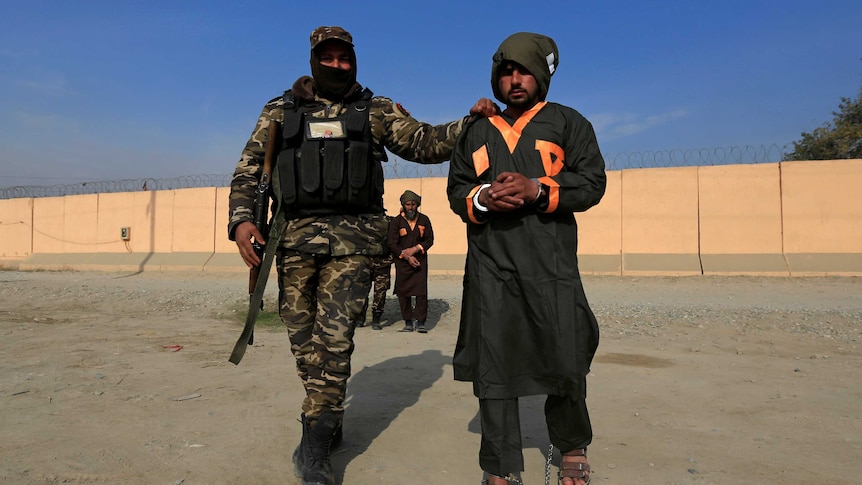 A captured and handcuffed Taliban insurgent is presented to the media by an Afghan soldier.
