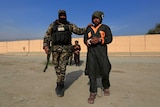 A captured and handcuffed Taliban insurgent is presented to the media by an Afghan soldier.