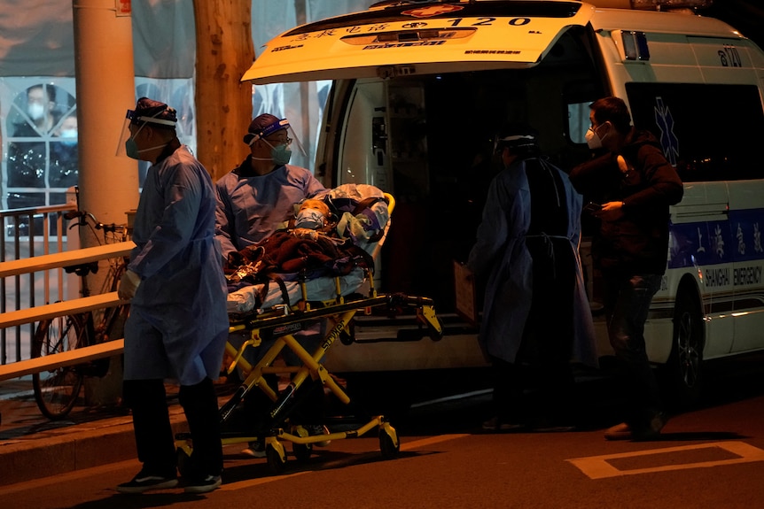 A woman on a stretcher is pushed along by people in blue medical suits. 