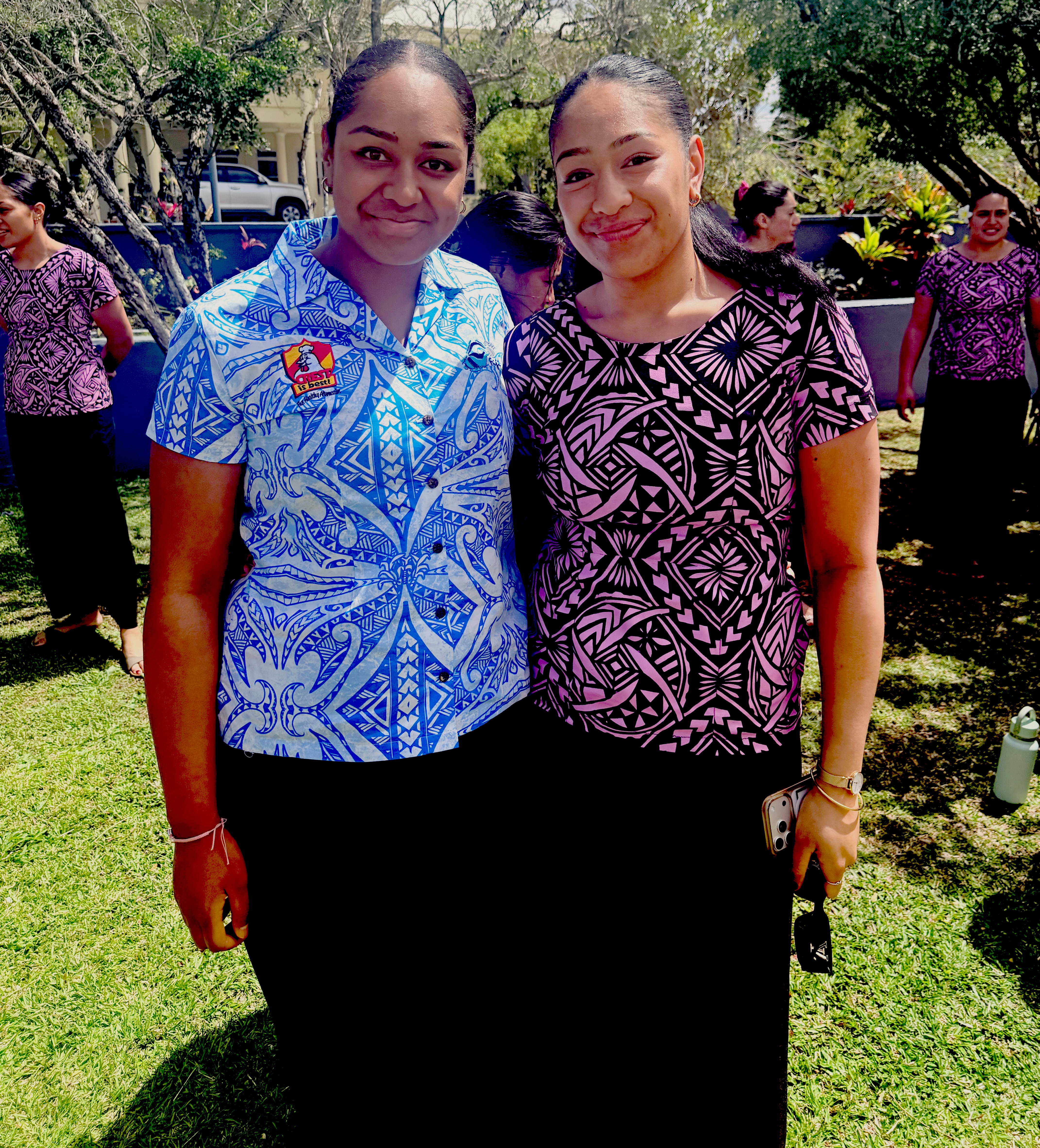 Two Pacific island women with hair tied back stand side by side looking at camera