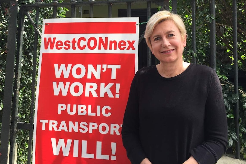 A woman standing outside a house, with a sign.