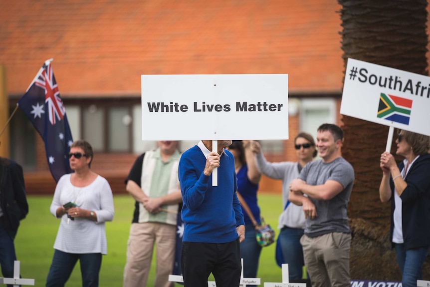 A man holds a White Lives Matter sign among a group of protestors outdoors.