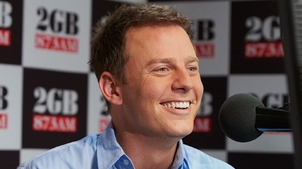 A man smiling with 2GB logos in the background.
