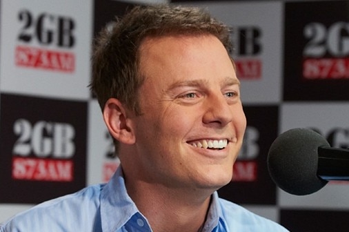 A man smiling with 2GB logos in the background.