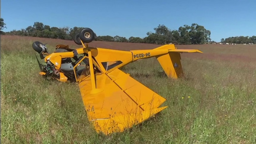 A yellow light plane on its back in a paddock