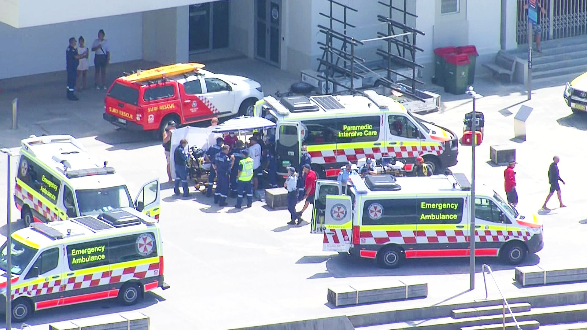 three ambulances out the front of a surf house at the beach with police and paramedics surrounding the cars