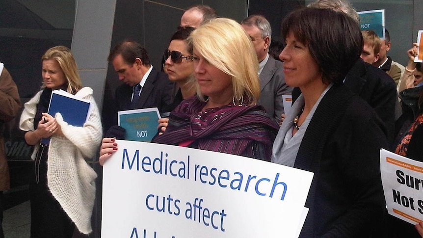 Protester holding sign saying 'Medical research cuts affect all Australians'.
